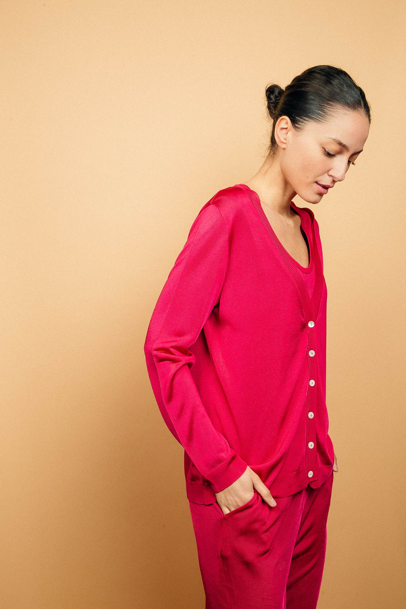 Cardigan rose fushia uni très lumineux en viscose, manches longues, encolure V, 6 boutons, finitions bords côtes. Coupe droite, fluide, porté en twin set avec le débardeur en viscose rose fushia et le pantalon en viscose rose fushia uni. Longueur couvrant le bas du dos.