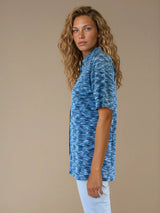 Chemise été femme, coloris bleu, manches courtes avec un imprimé strié.  La coupe avec un col est droite, les manches courtes arrivent au-dessus du coude. L'imprimé strié mélange des nuances de bleu et de blanc. Chemise en 100%viscose, lumineuse, fluide, très douce.
Vue profil.