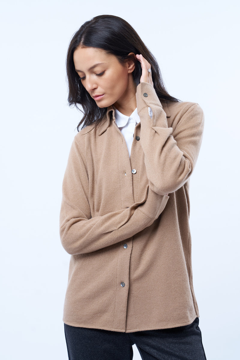 Chemise camel, manches longues, coupe droite, 100% cachemire  avec un col large et des poignets. Chemise portée en superposition sur un chemisier. Vue face.
