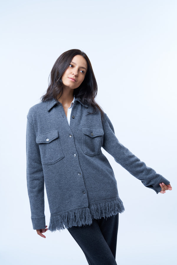 Chemise manches longues ou surchemise grise en cachemire, soie et mérinos. La chemise a 2 poches plaquées avec un rabat au niveau de la poitrine, est terminée dans le bas par une bande de franges en maille grise. Se porte également ouverte comme surchemise.