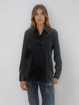 Chemise manches longues coloris noir en soie. Coupe légèrement cintrée avec 2 pinces dans le dos. Patte de boutonnage recouverte.  Vue face.