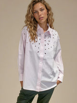 Chemise manches longues en 100% coton rayé rose et blanc. Petit col et forme trapèze avec des broderies ajourées au niveau du buste. Vue face.
