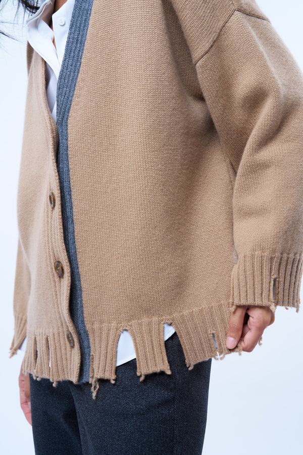 Gilet manches longues coloris camel avec une coupe oversize. Sur le long de l'encolure côté gauche : bande  de couleur grise. Le gilet présente des détails déchirés irréguliers aux bas des manches et sur tout le pourtour du bas . Emmanchures basses. Vue détails encolure. Composition: 42%cachemire, 8% soie, 50%mérinos.