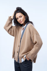 Gilet manches longues coloris camel avec une coupe oversize. Sur le long de l'encolure côté gauche : bande  de couleur grise. Le gilet présente des détails déchirés irréguliers aux bas des manches et sur tout le pourtour du bas . Emmanchures basses. Composition: 42%cachemire, 8% soie, 50%mérinos.