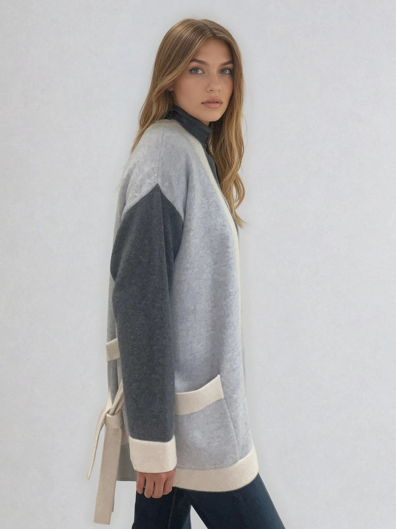 Veste tricolore en cachemire, soie, mérinos. Les manches sont gris anthracite, tous les contours sont en beige et le corps de la veste est en gris clair. Emmanchures basses. Le gilet a 2 poches plaquées gris clair, beige et une ceinture beige. Vue profil.
