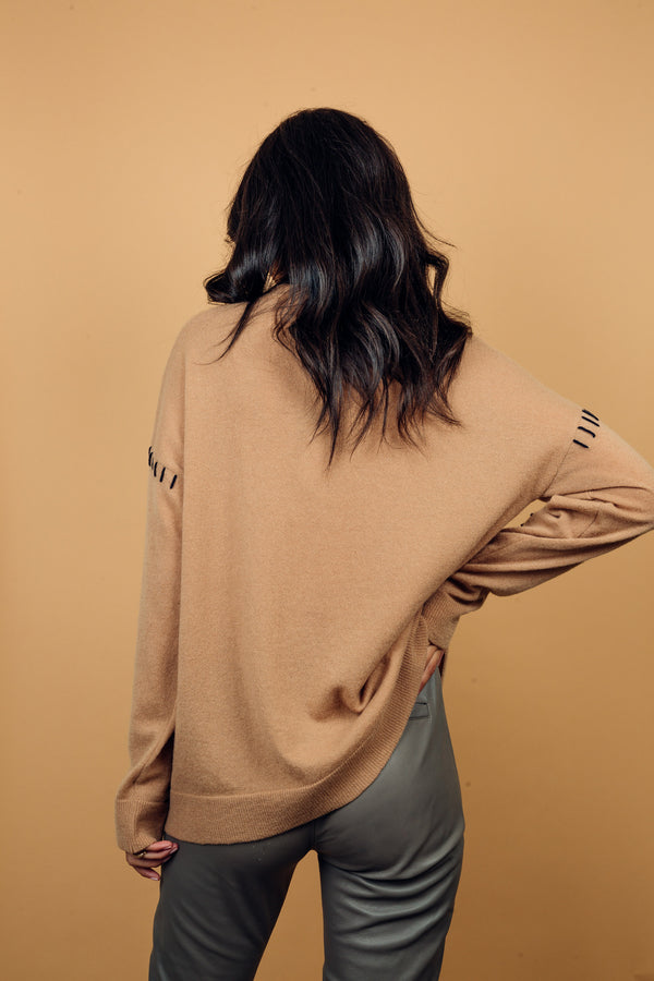 Gilet manches longues coloris camel avec une coupe droite. Les emmanchures sont basses, finitions côtes. Particularité de ce gilet: il est comme reprisé sur un côté du col, des coutures emmanchures, et une partie du bas avec un fil marine, effet rapiécé. Vue dos.
45%cachemire et 55% mérinos