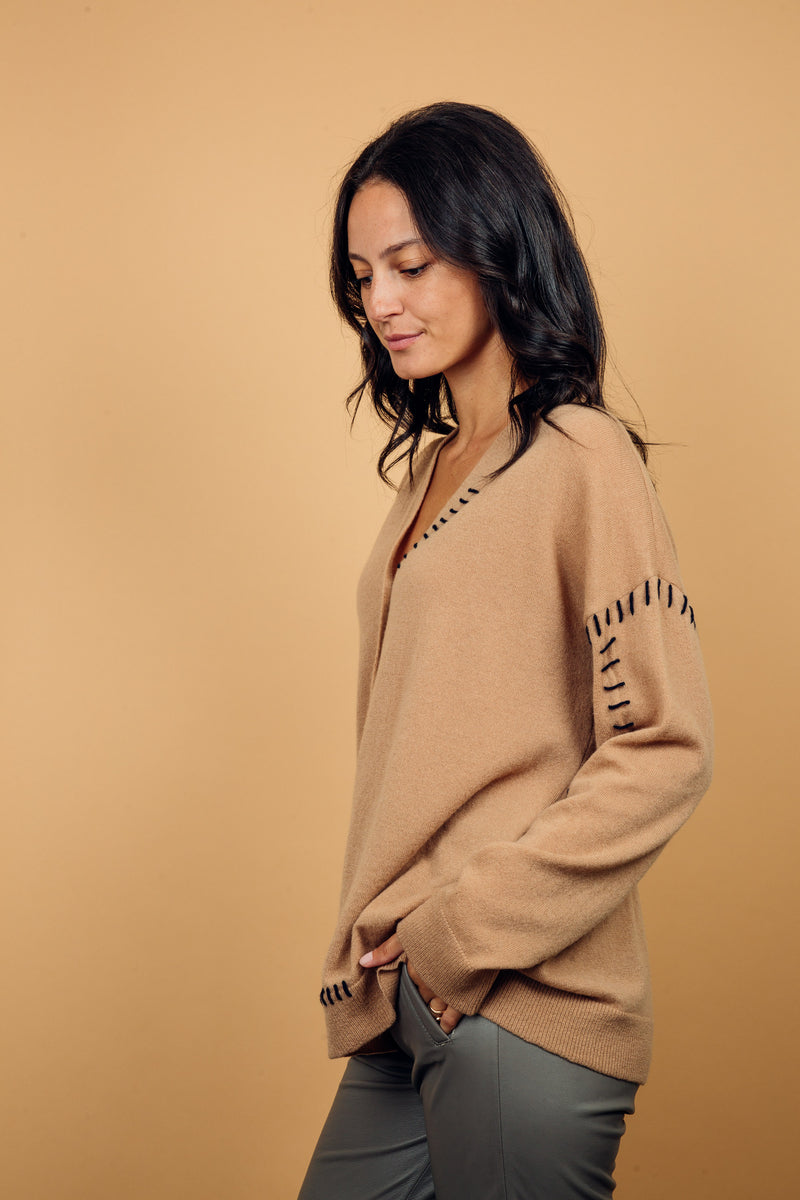 Gilet manches longues coloris camel avec une coupe droite. Les emmanchures sont basses, finitions côtes. Particularité de ce gilet: il est comme reprisé sur un côté du col, des coutures emmanchures, et une partie du bas avec un fil marine, effet rapiécé. Vue profil.
45%cachemire et 55% mérinos