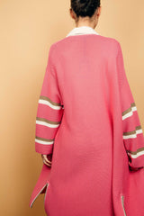 Gilet long rose malabar tricoté au point mousse. Coupe confort, 80% de coton et 15% de cachemire. Les emmanchures sont basses, la manche est large, pas resserrée et a 3 bandes rayées espacées, chacune étant composée d'une ligne écru collée à une ligne taupe. Bande également présente sur tout le pourtour du gilet et sur les fentes de chaque côté. Vue dos.