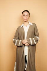Gilet long taupe tricoté au point mousse. Coupe confort, 80% de coton et 15% de cachemire. Les emmanchures sont basses, la manche est large, pas resserrée et a 3 bandes rayées espacées, chacune étant composée d'une ligne écru collée à une ligne beige. Bande également présente sur tout le pourtour du gilet et sur les fentes de chaque côté.