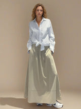 Jupe longue beige en 100% coton, la coupe est ample et se termine par une finition ballon. Taille élastiquée avec 2 poches italiennes sur les côtés.
Vue face.