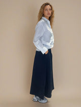 Jupe longue marine en 100% coton, la coupe est ample et se termine par une finition ballon. Taille élastiquée avec 2 poches italiennes sur les côtés.
Vue profil.
