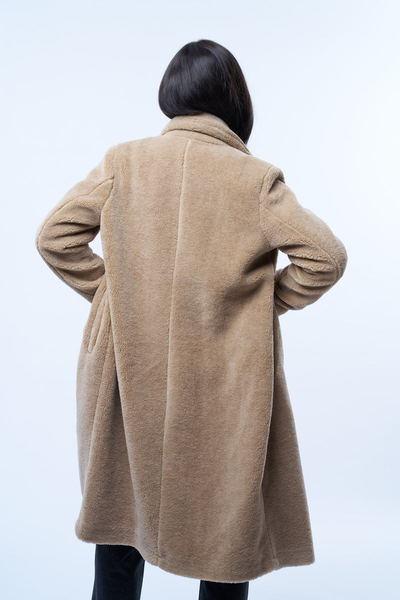 Manteau beige en fausse fourrure effet bouclé. 100% polyester. Coupe droite façon pardessus croisé, fermé par 2 boutons. Col tailleur, 2 poches cotés. Vue dos.