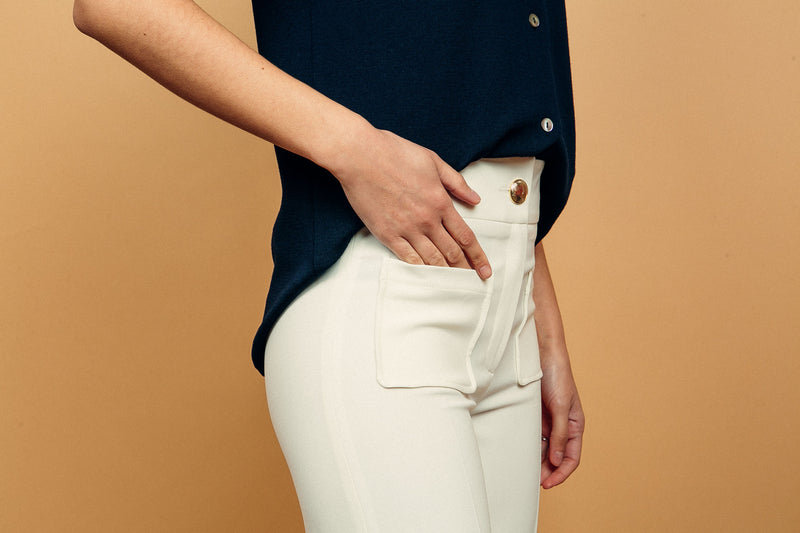 Pantalon BRIGITTE coloris blanc, coupe large sur toute la jambe, 2 poches plaquées sur le devant. Taille placée avec bouton doré. Texture douce et fluide 95% viscose et 5% élasthanne. Vue poches.