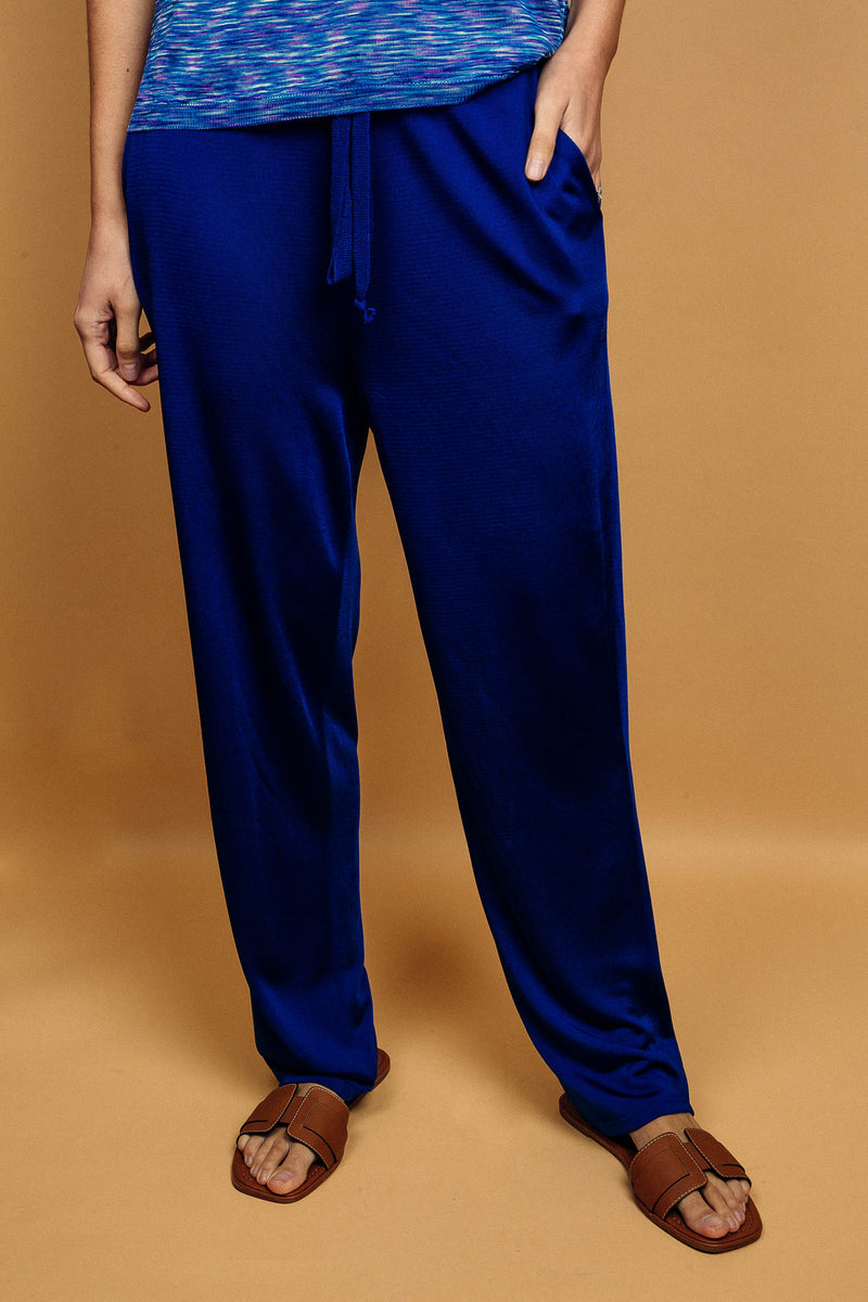 Pantalon bleu uni très lumineux, la taille est élastiquée ajustée par un lacet en viscose, il a 1 poche de chaque côté.  La forme est droite, le bas n'est pas resserré. Il est en 100% viscose ce qui  apporte au pantalon de la fluidité, de la brillance et un confort maxi.