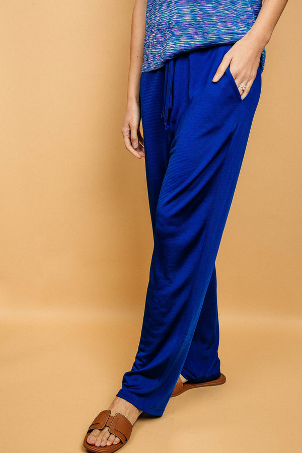 Pantalon bleu uni très lumineux, la taille est élastiquée ajustée par un lacet en viscose, il a 1 poche de chaque côté.  La forme est droite, le bas n'est pas resserré. Il est en 100% viscose ce qui  apporte au pantalon de la fluidité, de la brillance et un confort maxi.