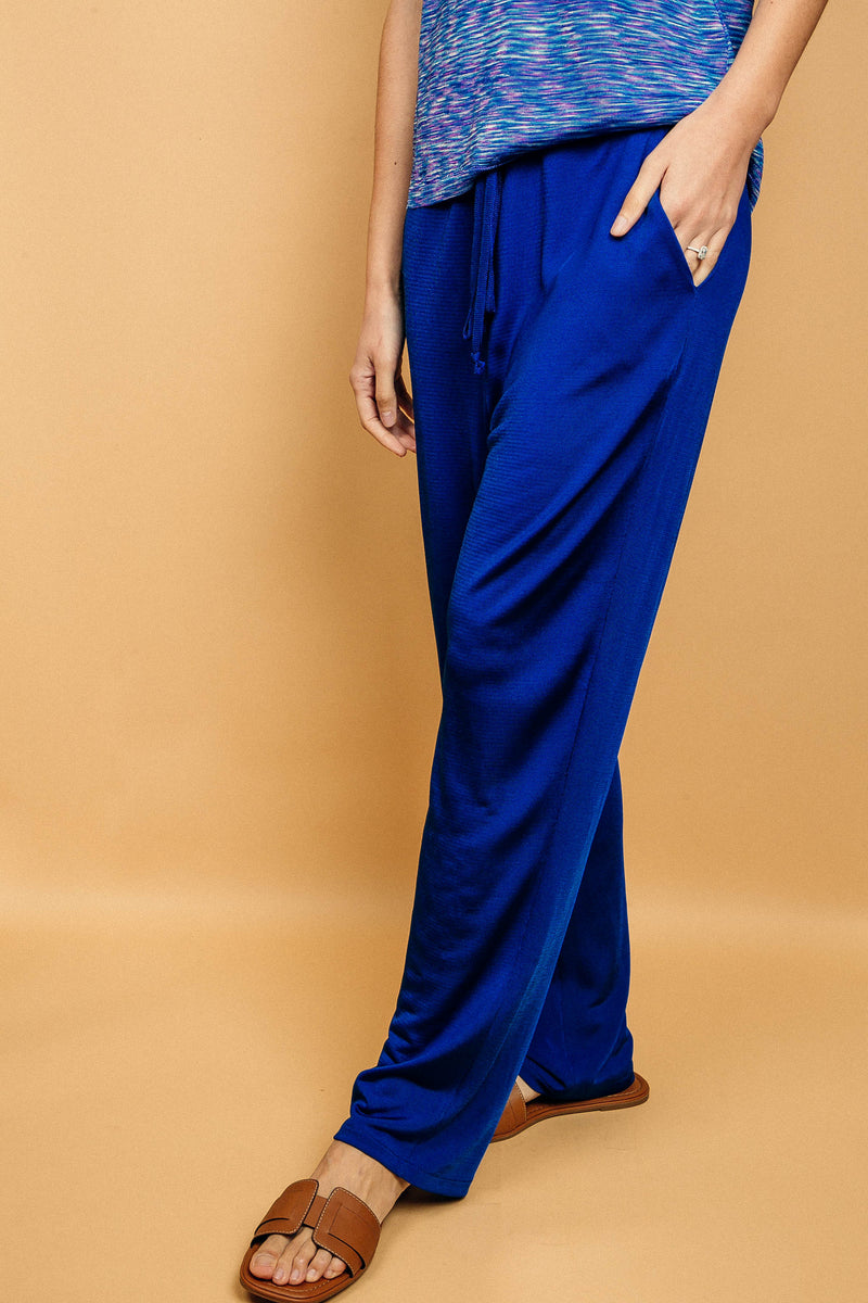 Pantalon bleu uni très lumineux, la taille est élastiquée ajustée par un lacet en viscose, il a 1 poche de chaque côté.  La forme est droite, le bas n'est pas resserré. Il est en 100% viscose ce qui  apporte au pantalon de la fluidité, de la brillance et un confort maxi.