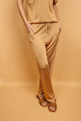Pantalon doré miel uni très lumineux, la taille est élastiquée ajustée par un lacet en viscose, il a 1 poche de chaque côté.  La forme est droite, le bas n'est pas resserré. Il est en 100% viscose ce qui  apporte au pantalon de la fluidité, de la brillance et un confort maxi.