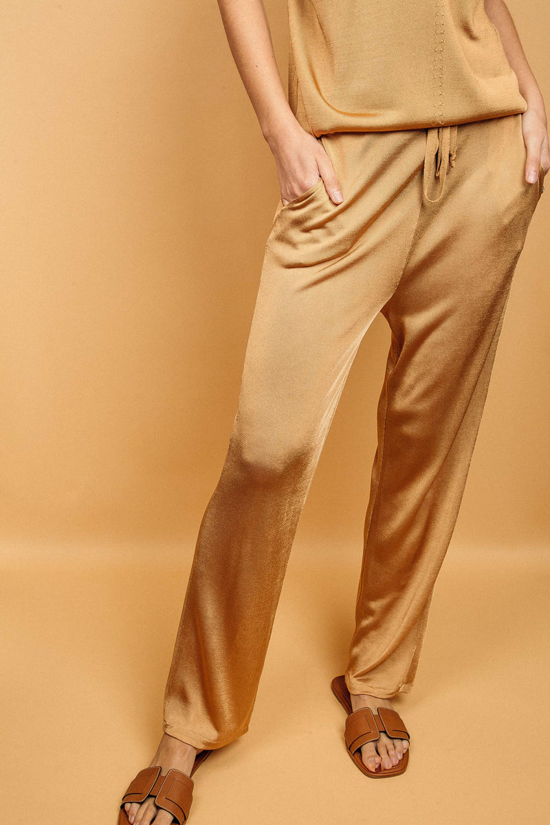 Pantalon doré miel uni très lumineux, la taille est élastiquée ajustée par un lacet en viscose, il a 1 poche de chaque côté.  La forme est droite, le bas n'est pas resserré. Il est en 100% viscose ce qui apporte au pantalon de la fluidité, de la brillance et un confort maxi.