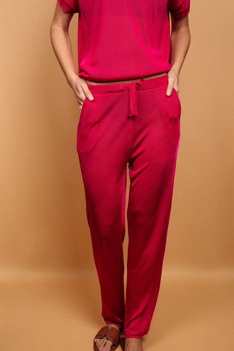 Pantalon rose fushia uni très lumineux, la taille est élastiquée ajustée par un lacet en viscose, il a 1 poche de chaque côté.  La forme est droite, le bas n'est pas resserré. Il est en 100% viscose ce qui apporte au pantalon de la fluidité, de la brillance et un confort maxi.