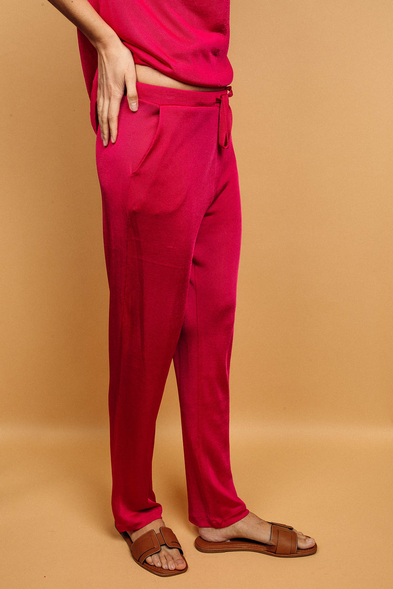 Pantalon rose fushia uni très lumineux, la taille est élastiquée ajustée par un lacet en viscose, il a 1 poche de chaque côté.  La forme est droite, le bas n'est pas resserré. Il est en 100% viscose ce qui apporte au pantalon de la fluidité, de la brillance et un confort maxi. Vue profil.