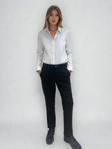 Pantalon noir de ville avec une forme droite. Poches italiennes et dos élastiqué. Détail de la patte rehaussée de fil lurex au niveau des passants. Vue face.