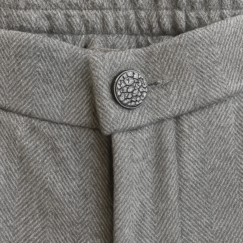 Pantalon droit gris avec un motif chevrons fines rayures. La taille dans le dos est élastiquée. Vue du bouton strass.
