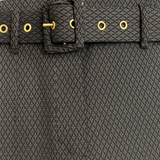 Pantalon de forme bootcut souple et confortable: jambe légèrement appuyée et bas évasé. Le tissu marron est imprimé de petits croisillons beige et vert. La ceinture de ce leggings est recouverte du même tissu, les œillets sont dorés ainsi que le bouton. Esprit années 70's. Le tissu est composé de 69% polyester, 27% rayon, 4% élasthanne. Vue ceinture attachée.