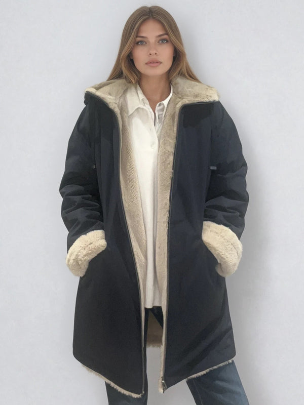 Parka marine avec capuche doublée en 100% polyester réversible avec d'un côté une face déperlante marine et de l'autre une face façon fausse fourrure beige. Elle se ferme par un zip, a 2 poches zippées côté déperlant . Le bas des manches se retournent,  elle a une coupe droite et arrive à mi-cuisses. Vue face.