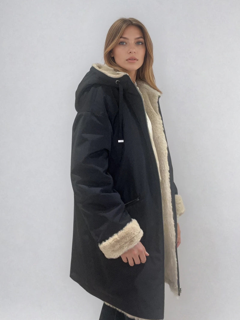 Parka marine avec capuche doublée en 100% polyester réversible avec d'un côté une face déperlante marine et de l'autre une face façon fausse fourrure beige. Elle se ferme par un zip, a 2 poches zippées côté déperlant . Le bas des manches se retournent,  elle a une coupe droite et arrive à mi-cuisses. Vue profil.
