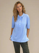 Polo femme d'été coloris ciel en 83% viscose et 17% nylon: fluide, coupe large et longue fendue sur les côtés. Le polo a un petit col qui s'ouvre sur 3 boutons, les manches courtes couvrent les avant-bras. Vue face.