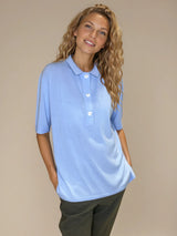 Polo femme d'été coloris ciel en 83% viscose et 17% nylon: fluide, coupe large et longue fendue sur les côtés. Le polo a un petit col qui s'ouvre sur 3 boutons, les manches courtes couvrent les avant-bras. Vue face.