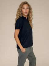 Polo femme manches courtes coloris noir. Le polo est en 100% polyester, il a une maille texturée en nid d'abeille. Petit col sur une ouverture V. Forme droite, maille légère et aérienne.
Vue profil.