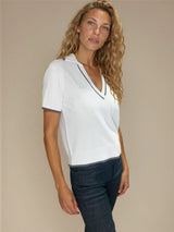 Polo coloris blanc pour femme avec manches courtes, esprit tennis. L' encolure V est rehaussée par une rayure grise, détail présent également sur le bas des manches. Petit col.
100%viscose.
Vue profil.