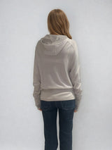 Pull encolure ronde  souple avec capuche coloris beige en 100% laine mérinos. Manches longues terminées par un long poignet côtelé avec une ouverture pour y glisser le pouce comme une mitaine. Emmanchures raglan, large bande côtelée sur le bas. Vue dos.