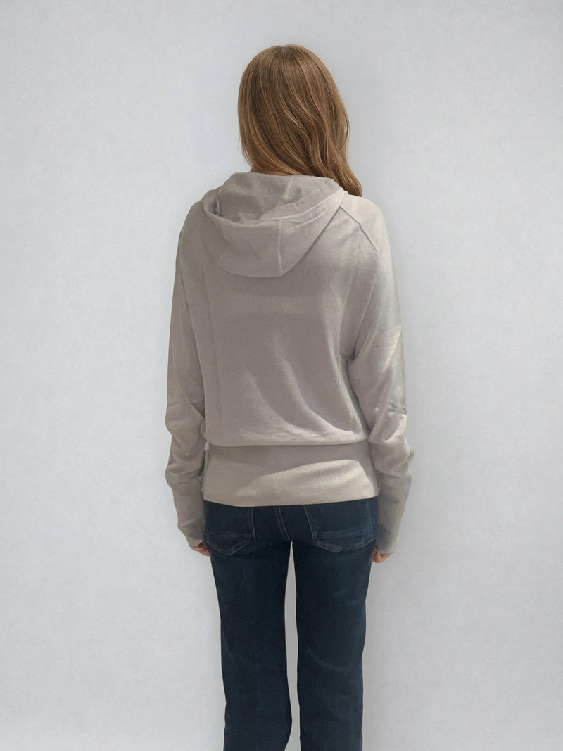 Pull encolure ronde  souple avec capuche coloris beige en 100% laine mérinos. Manches longues terminées par un long poignet côtelé avec une ouverture pour y glisser le pouce comme une mitaine. Emmanchures raglan, large bande côtelée sur le bas. Vue dos.