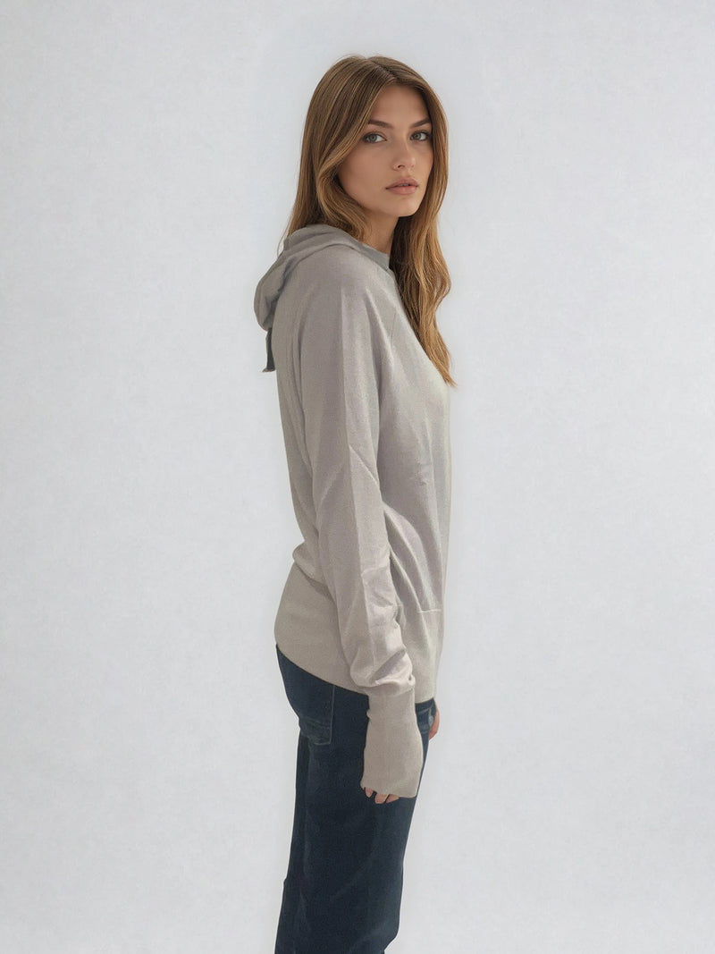 Pull encolure ronde souple avec capuche coloris beige en 100% laine mérinos. Manches longues terminées par un long poignet côtelé avec une ouverture pour y glisser le pouce comme une mitaine. Emmanchures raglan, large bande côtelée sur le bas. Vue profil.