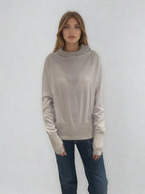 Pull encolure ronde souple avec capuche coloris beige en 100% laine mérinos. Manches longues terminées par un long poignet côtelé avec une ouverture pour y glisser le pouce comme une mitaine. Emmanchures raglan, large bande côtelée sur le bas. Vue face.
