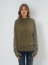 Pull encolure ronde souple avec capuche coloris kaki en 100% laine mérinos. Manches longues terminées par un long poignet côtelé avec une ouverture pour y glisser le pouce comme une mitaine. Emmanchures raglan, large bande côtelée sur le bas. Vue face.