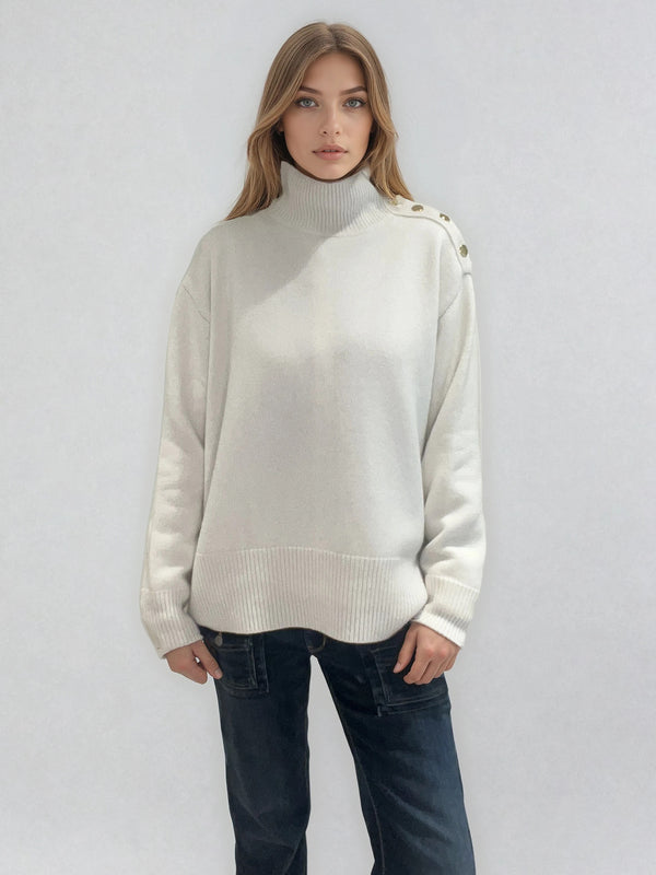 Pull écru  avec un col cheminée  en 42% cachemire , 8% soie et 50% mérinos. Sur l'épaule gauche se trouve une patte ornée de 5 boutons dorés patinés, le pull peut se déboutonner. Les emmanchures sont basses , la forme est confort et large. Finitions côtes.