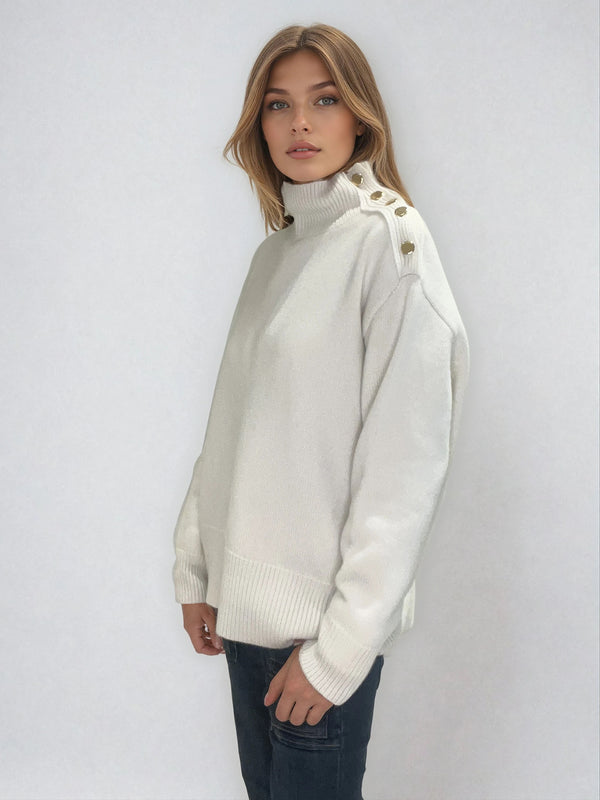 Pull écru  avec un col cheminée  en 42% cachemire , 8% soie et 50% mérinos. Sur l'épaule gauche se trouve une patte ornée de 5 boutons dorés patinés, le pull peut se déboutonner. Les emmanchures sont basses , la forme est confort et large. Finitions côtes.