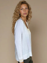 Pull manches longues col rond. Le pull est blanc, a un col beige très arrondi rehaussé d'une bande jaune pale, détail présent aussi sur le bas des manches. Coupe souple avec une asymétrie sur les côtés.
Composition: 83%viscose et 17% nylon. Vue profil.