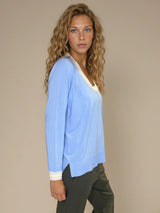 Pull manches longues col rond. Le pull est ciel, a un col beige très arrondi rehaussé d'une bande jaune, détail présent aussi sur le bas des manches. Coupe souple avec une asymétrie sur les côtés.
Composition: 83%viscose et 17% nylon. Vue profil.