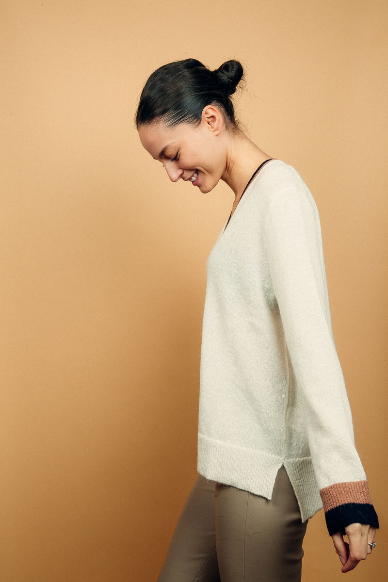 Pull EMILIA fond écru avec col V et bas de manches longues bicolores: bandes camel et marine. Fentes côtés asymétriques. Composition: 50%mohair, 36%nylon, 14%laine.
