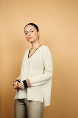 Pull EMILIA fond écru avec col V et bas de manches longues bicolores: bandes camel et marine. Fentes côtés asymétriques. Composition: 50%mohair, 36%nylon, 14%laine.
