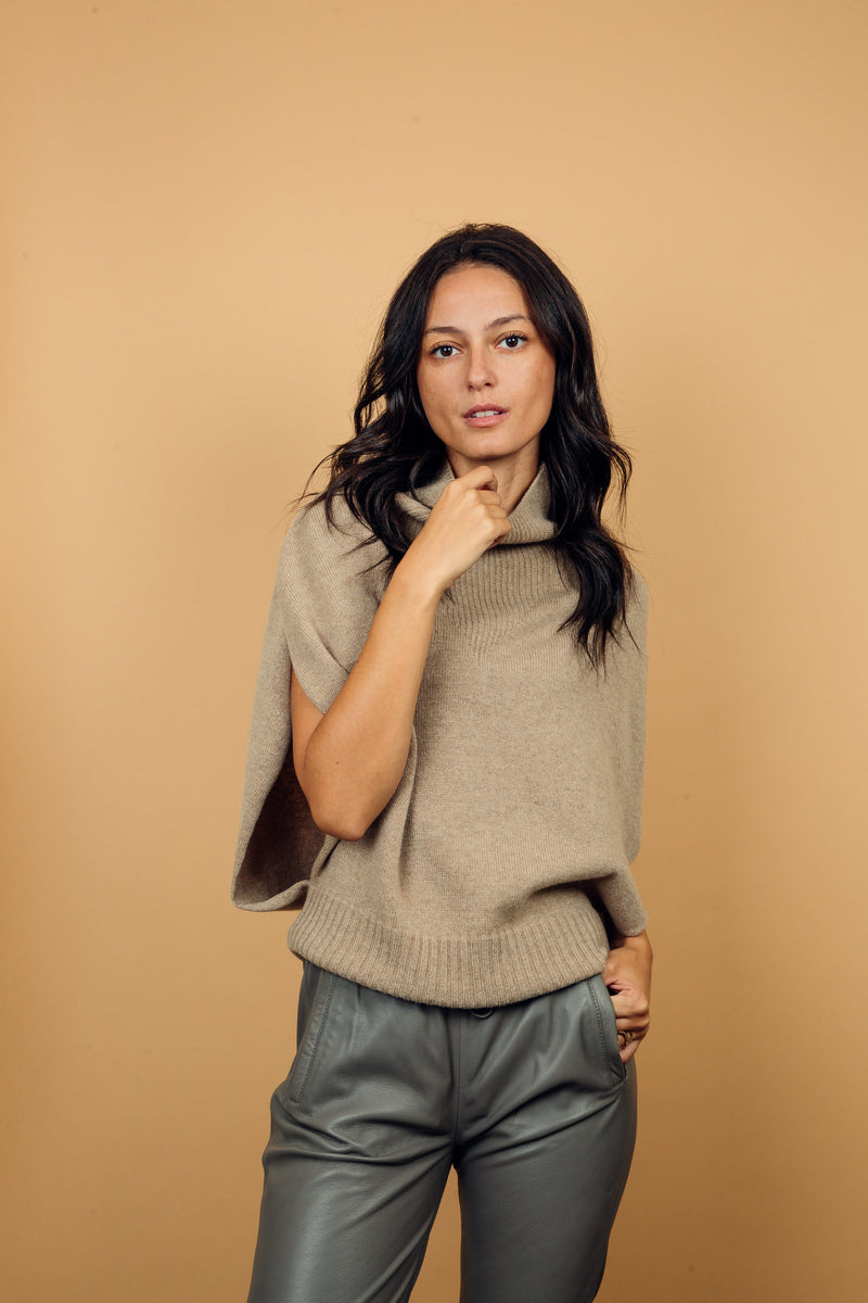 Pull col roulé sans manches beige, coupe oversize  avec une ouverture de haut en bas sur les côtés jusqu'au début des côtes de la taille. Le col est haut et souple, l'avant -bras est légèrement recouvert. Mélange de cachemire, soie et mérinos.