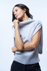 Pull col roulé sans manches gris clair, coupe oversize  avec une ouverture de haut en bas sur les côtés jusqu'au début des côtes de la taille. Le col est haut et souple, l'avant -bras est légèrement recouvert. Mélange de cachemire, soie et mérinos.