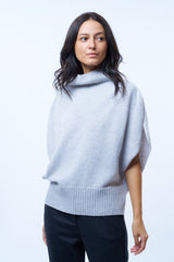 Pull col roulé sans manches gris clair, coupe oversize  avec une ouverture de haut en bas sur les côtés jusqu'au début des côtes de la taille. Le col est haut et souple, l'avant -bras est légèrement recouvert. Mélange de cachemire, soie et mérinos.