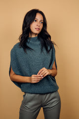 Pull col roulé sans manches gris, coupe oversize  avec une ouverture de haut en bas sur les côtés jusqu'au début des côtes de la taille. Le col est haut et souple, l'avant -bras est légèrement recouvert. Mélange de cachemire, soie et mérinos.