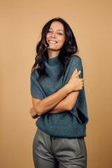 Pull col roulé sans manches gris, coupe oversize  avec une ouverture de haut en bas sur les côtés jusqu'au début des côtes de la taille. Le col est haut et souple, l'avant -bras est légèrement recouvert. Mélange de cachemire, soie et mérinos.