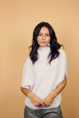 Pull col roulé sans manches rose clair, coupe oversize  avec une ouverture de haut en bas sur les côtés jusqu'au début des côtes de la taille. Le col est haut et souple, l'avant -bras est légèrement recouvert. Mélange de cachemire, soie et mérinos.